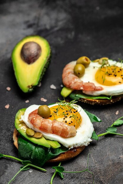 Breakfast sanwich with wholemeal bread soft fried egg spinach avocado shrimps on dark background Ketogenic breakfast superfood concept Healthy clean eating Top view