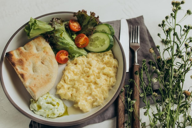 Breakfast of scrambled eggs bread and vegetables served on a flat plate