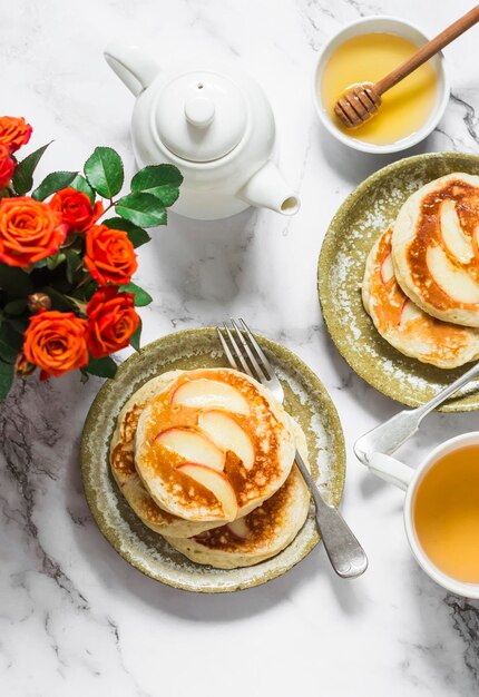 Breakfast served pancakes with apples green tea a bouquet of roses on a light marble background top view