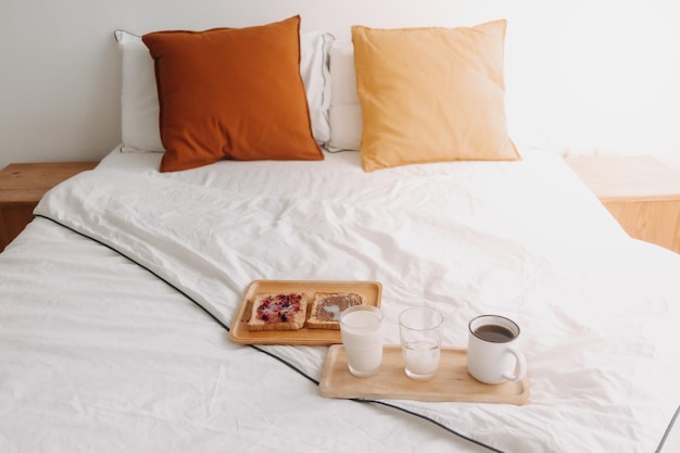 Breakfast set of breads and jam with milk and coffee on white bed