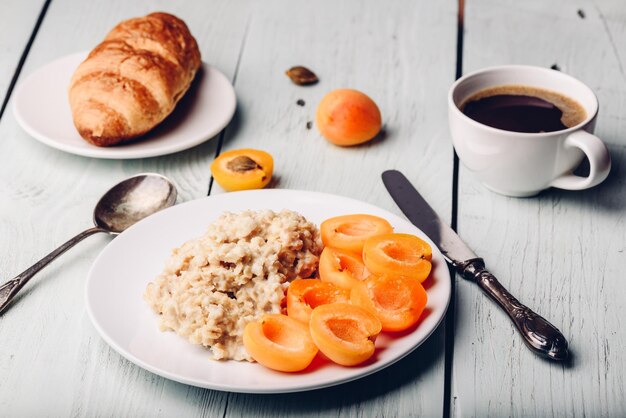 Foto set per la colazione. porridge con albicocca affettata, tazza di caffè, bicchiere di succo di pompelmo e croissant