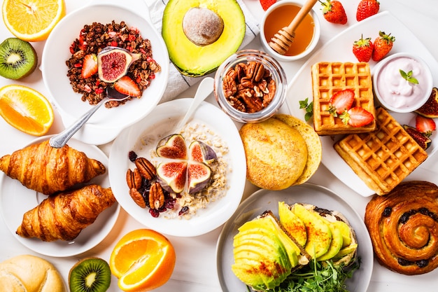 Photo breakfast table with avocado toast, oatmeal, waffles, croissants on white