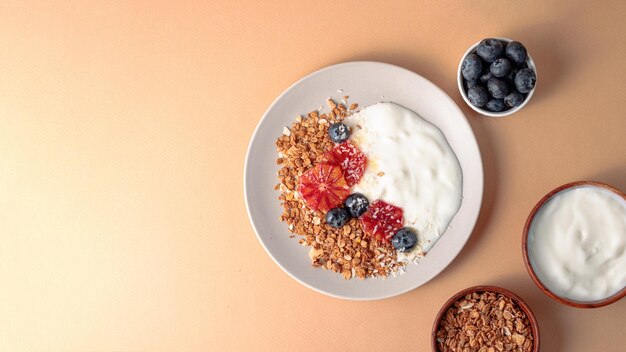 Photo breakfast table with granola bowl with greek yogurt decorated by blood oranges blueberry and coconut beige background ingredient for breakfast top view with copyspace