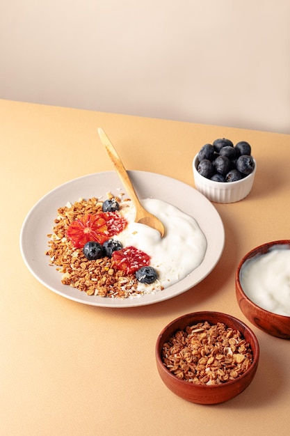 Photo breakfast table with granola bowl with greek yogurt decorated by blood oranges blueberry and coconut beige background ingredient for breakfast top view