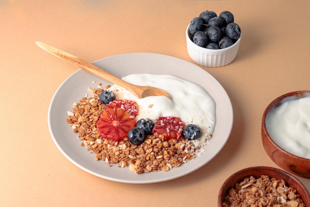 Breakfast table with granola bowl with greek yogurt decorated by blood oranges blueberry and coconut beige background ingredient for breakfast top view