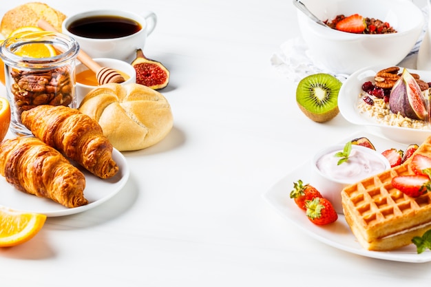 Breakfast table with oatmeal, waffles, croissants and fruits 