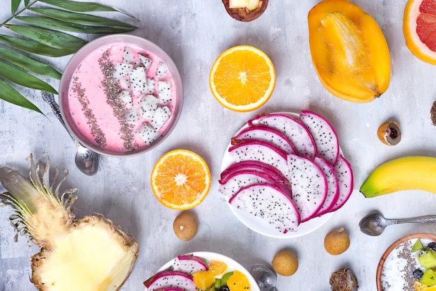 Breakfast table with yogurt strawberry smoothie bowls and fresh tropic fruits on a gray stone background. Acai bowl of wild berry and fruits smoothie bowl, flat lay