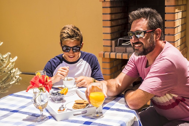 Breakfast time in the morning for beautiful caucasian family in the terrace outdoor at home cheerful happy people and love between father and son in leisure activity