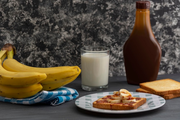 Breakfast of toast with banana and caramel accompanied by a glass of milk on a table