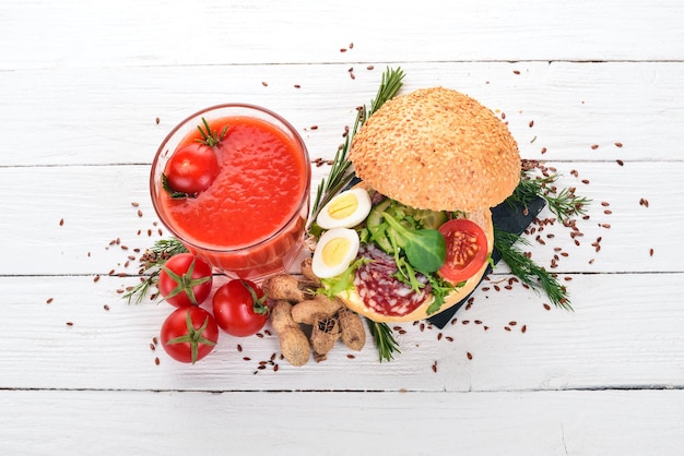 朝食トマトジュースとサラミと野菜のハンバーガー木製の背景に上面図コピースペース