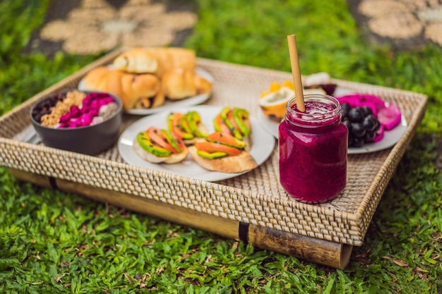 Breakfast on a tray with fruit buns avocado sandwiches smoothie bowl standing on the grass