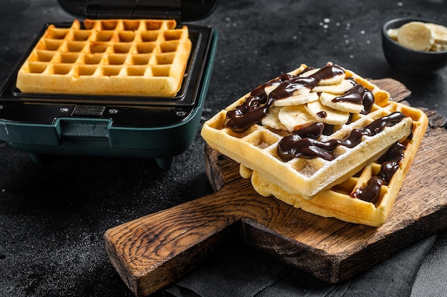 Breakfast with Belgian waffles, banana and Chocolate Syrup. Black background. Top view.