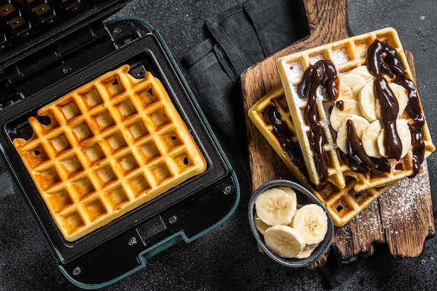 Breakfast with Belgian waffles banana and Chocolate Syrup Black background Top view