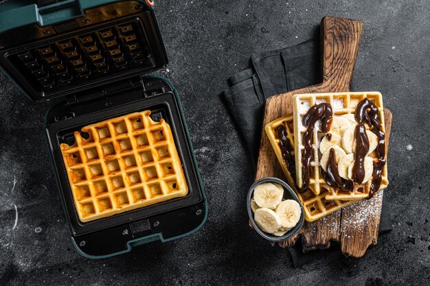 Photo breakfast with belgian waffles banana and chocolate syrup black background top view