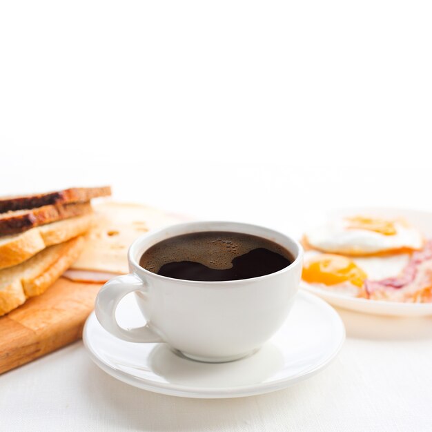 Breakfast with coffee, toasted bread, eggs, bacon, cold cuts and cheese on white background