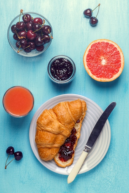 Breakfast with croissant, jam, fruit and juice.