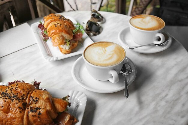 Breakfast with croissant sandwiches and coffee on table
