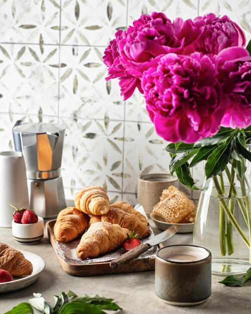 Фото Завтрак с круассанами, кофе, пионами, цветочной медовой композицией на плиточном фоне