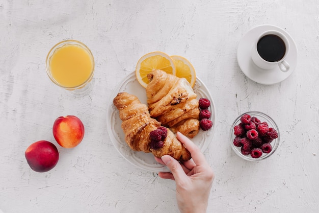 Breakfast with croissants, a cup of coffee, raspberries and orange juice top view