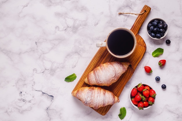 Breakfast with croissants and fresh fruits, top view.