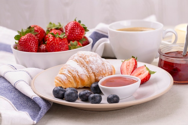 Breakfast with a cup of coffee, fresh croissant, strawberries and blueberries and juicy oranges