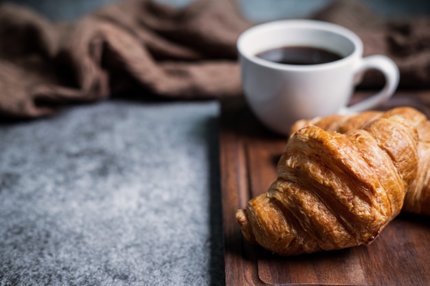 Breakfast with fresh croissants and cup of black coffee on wooden board