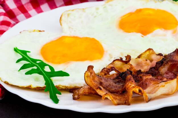 Colazione con uova fritte, pancetta e insalata di rucola su sfondo di pietra scura.