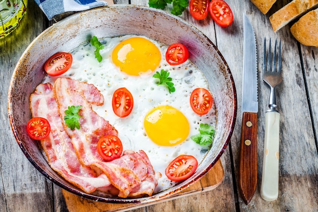 Breakfast with fried eggs bacon tomatoes and parsley on rustic table