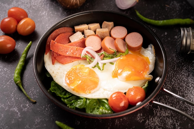 breakfast with fried eggs sausage and ham in a pan with tomatoes chili and basil