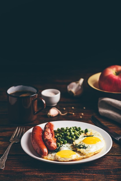 Breakfast with fried eggs, sausages and green peas on white plate