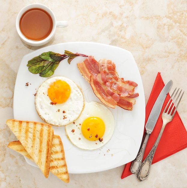 대리석 표면에 튀긴 계란, 토스트, 베이컨, 차와 함께 아침 식사
