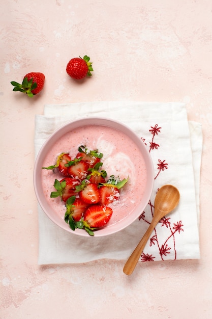 Colazione con muesli, cocco e frullato di fragole in una ciotola su uno sfondo rosa chiaro. menu dieta primaverile. vista dall'alto.