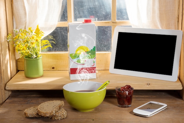 Breakfast with milk, bread, tablet and phone on the edge of a window