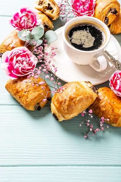 ブルーターコイズの表面にチョコレートとコーヒーカップが入ったミニ焼きたてのクロワッサンパンで朝食。コピースペース