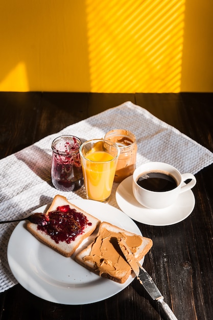 Breakfast with peanut butter and jam and a cup of coffee on a wooden table in the morning sun