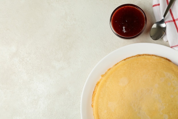 Breakfast with plate of thin pancakes and jam on white textured surface