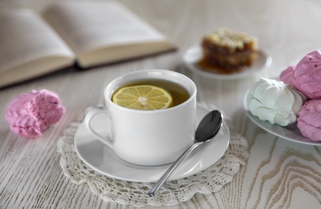 Foto colazione con marshmallow al ribes rosso e mela verde chiaro. tè al limone con tazza di tè bianco su uno sfondo bianco e sullo sfondo di un favo di libro aperto con lo stile di vita del miele di grano saraceno.