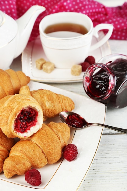 Breakfast with tea apple juice jam and fresh croissants on wooden table on bright background