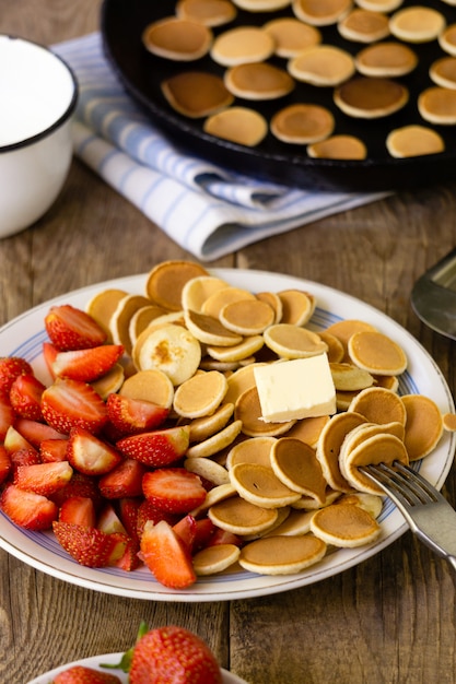 Faccia colazione con i pancake e la fragola piccoli d'avanguardia su un fondo di legno