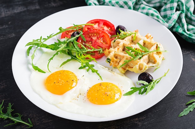 ズッキーニワッフル、目玉焼き、トマト、ブラックオリーブ、ルッコラを白地に朝食。前菜、軽食、ブランチ。健康的なベジタリアン料理。