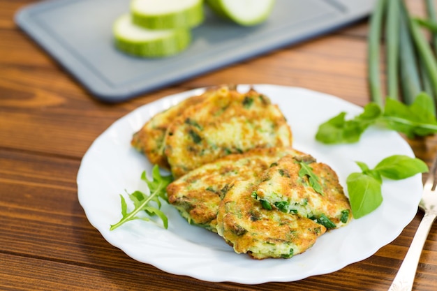 나무 테이블 에 있는 접시 에 초록 양파 를 넣은 zucchini fritters 의 아침 식사