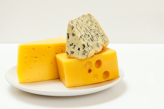 Кусочки французского полутвердого голубого сыра Фурм д'Амбер и польского сыра поразили фитнес на тарелке с белой поверхностью.