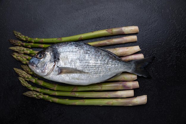 A bream fish on a black background with asparagus