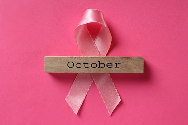 Breast cancer awareness ribbon and wooden block with text October on pink background