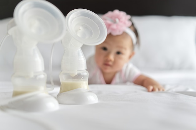 Il latte materno nelle bottiglie della pompa del latte sul letto con il piccolo bambino sveglio che striscia nel fondo.