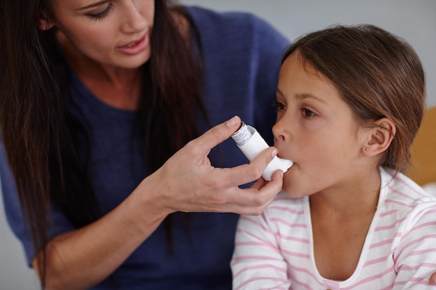 Photo breathe in honey shot of a caring mother giving her daughter an asthma pump at home