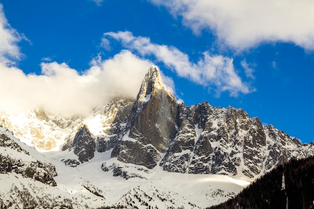 Vista aerea mozzafiato del picco di montagna del monte bianco coperto di neve splendente, ghiaccio e ghiacciai sotto il cielo blu con nuvole bianche gonfie sul lato francese delle alpi in una fredda giornata di sole invernale