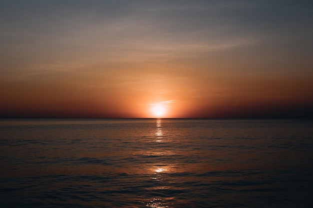 ビーチでの息を呑むような夏の夕日の眺め。真っ暗な海とその上のオレンジ色の空の素晴らしい夕日の風景と穏やかな波がその上を流れています。