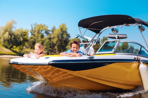 Breathtaking view. Joyful little siblings sitting on the bow of the boat and contemplating the view while smiling happily