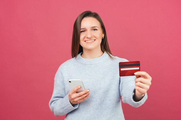 Brede glimlachende vrouw toont creditcard aan de camera terwijl ze haar telefoon vasthoudt